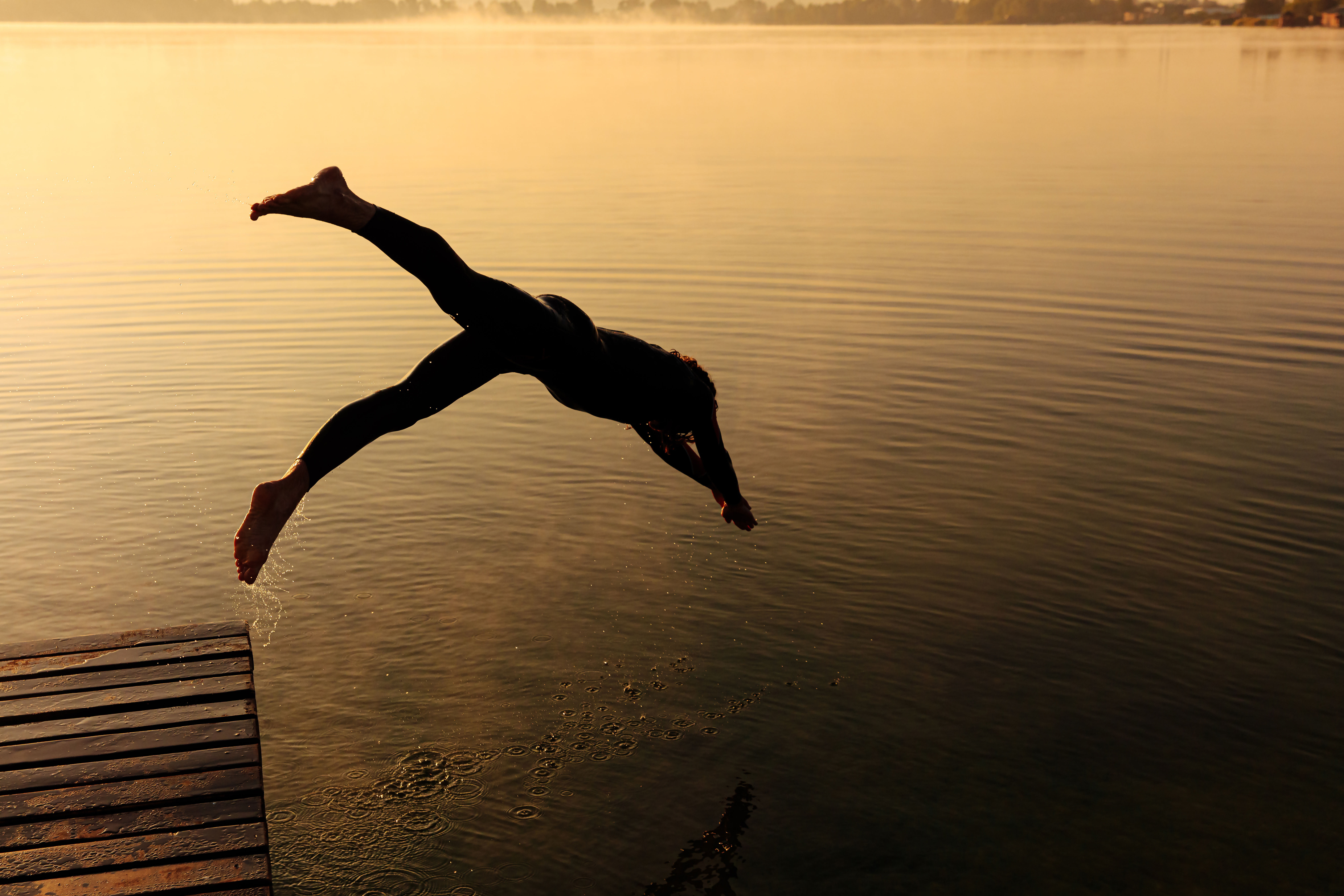 Silhouette of active sportsman dashing into foggy lake